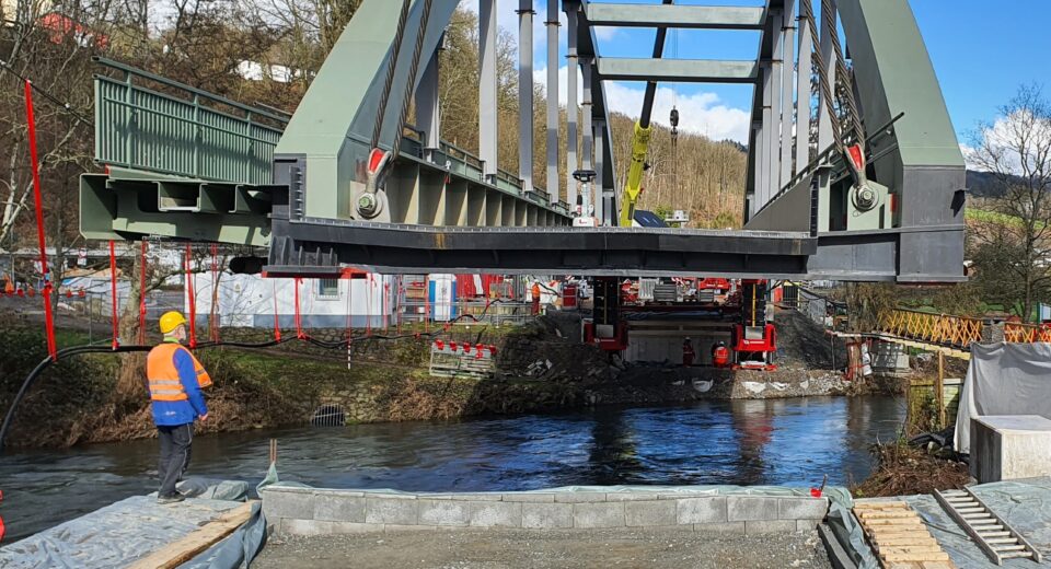 Kran hebt Stahlbrücke über den Fluss